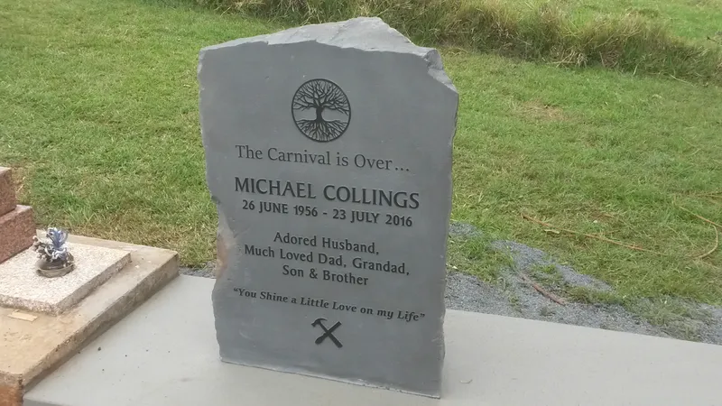 Upright local basalt headstone with a raised inscription and tree motif