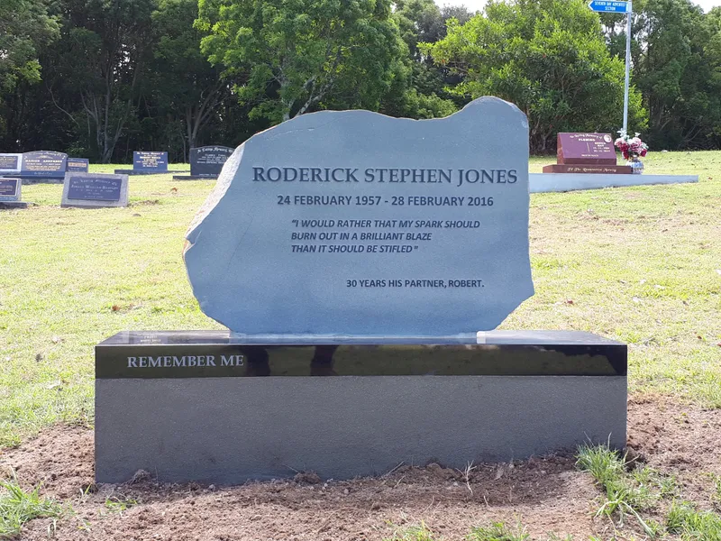 Natural basalt headstone with a raised inscription on a black granite base with an incised inscription
